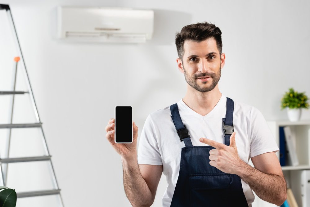 Reparador sonriente apuntando al telefono inteligente